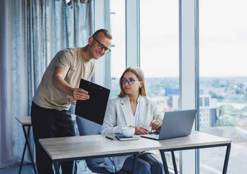 Colleague shows clipboard to seated coworker by window while business directory lists your business to attract more local customers